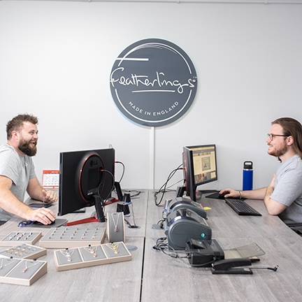 Two men sat at opposite desktops with screens on them talking about work