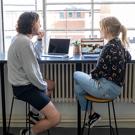 Two employees with laptops sitting at a bar desk that looks out of windows