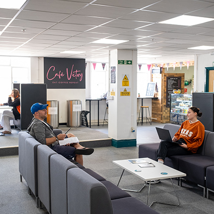 Two people sit in an open communal office space with sofas and tables