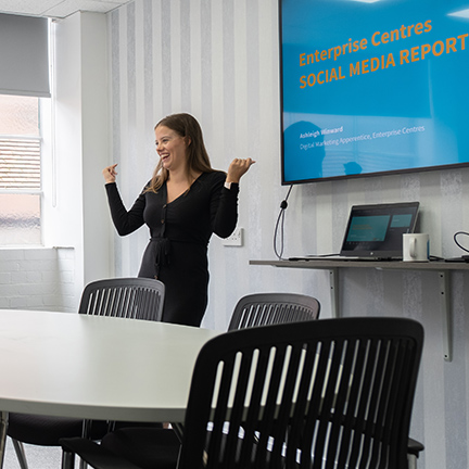 A lady giving a presentation in front of a large tv in a small meeting room