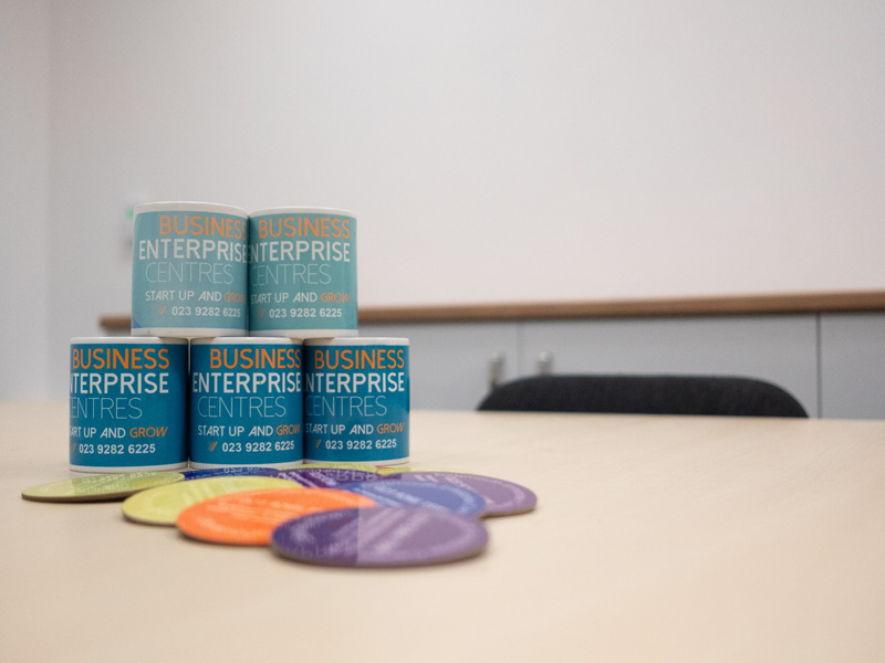 Portsmouth enterprise centre promotional mugs and coaster sets laid on a table