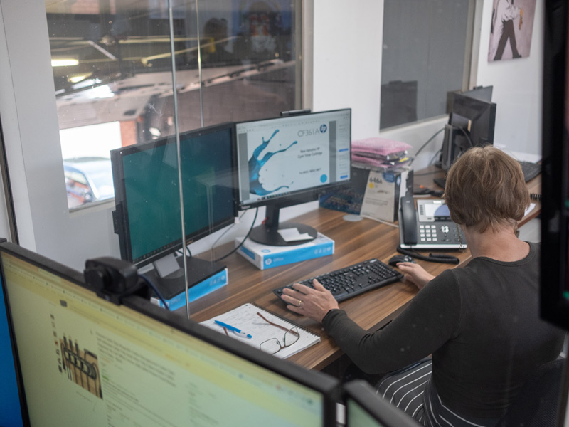 Lady working at desk with mulitple screens.